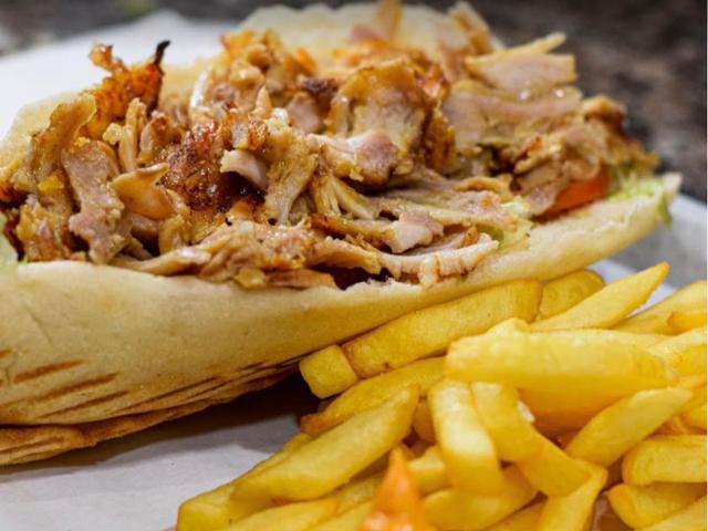 Kebab garni de viande grillée et de crudités, servi avec des frites et de la sauce.