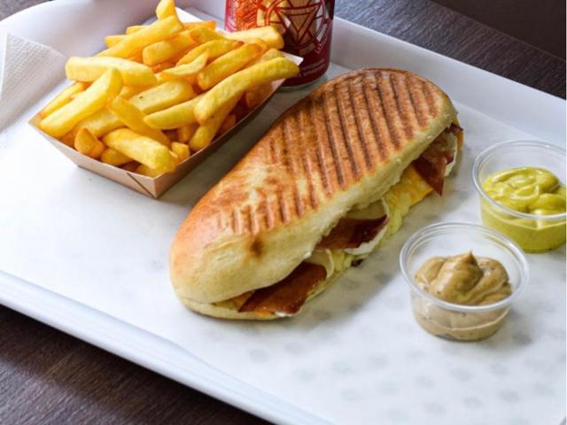 Sandwich dans un pain grillé, accompagné de frites et de sauces.
